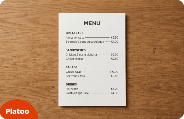 Carta impresa de una hoja de una cafetería, en cartulina blanca, con apartados de desayunos, sándwiches, ensaladas y bebidas, sobre una mesa de madera