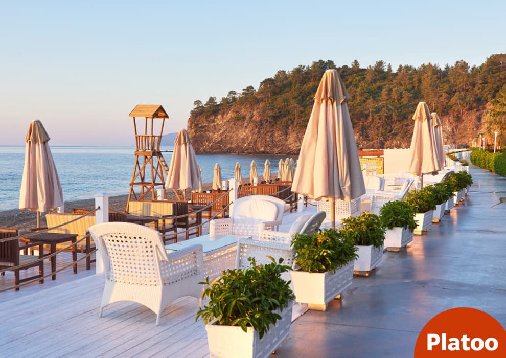 Terrasse de restaurant en bord de mer avec fauteuils en rotin blanc et parasols au coucher du soleil, prête pour la saison touristique
