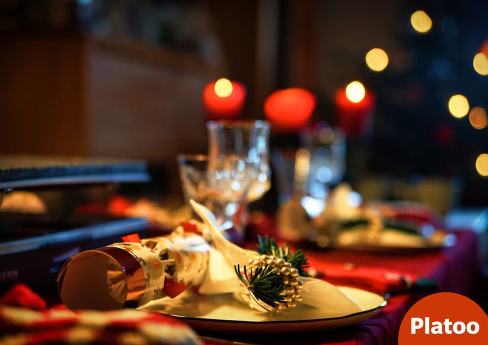 Slavnostně prostřený restaurační stůl na Silvestra s vystřelovací bonboniérou, větvičkou jedle na talíři, křišťálovými sklenicemi a červenými svíčkami