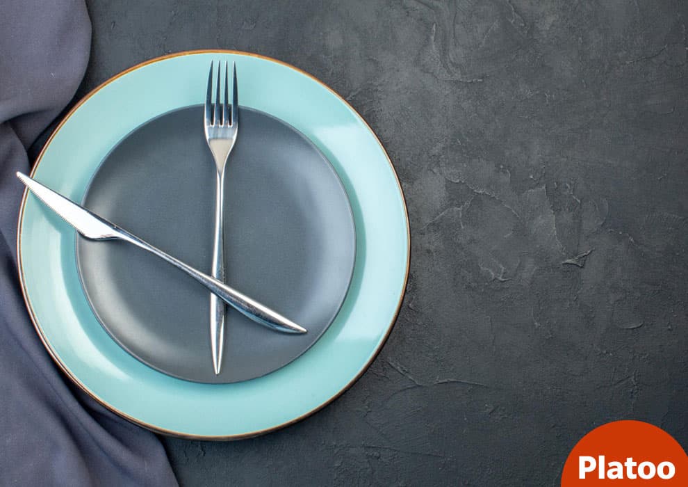 A grey plate on a light blue plate with a crossed knife and fork, beside a grey napkin on a dark table