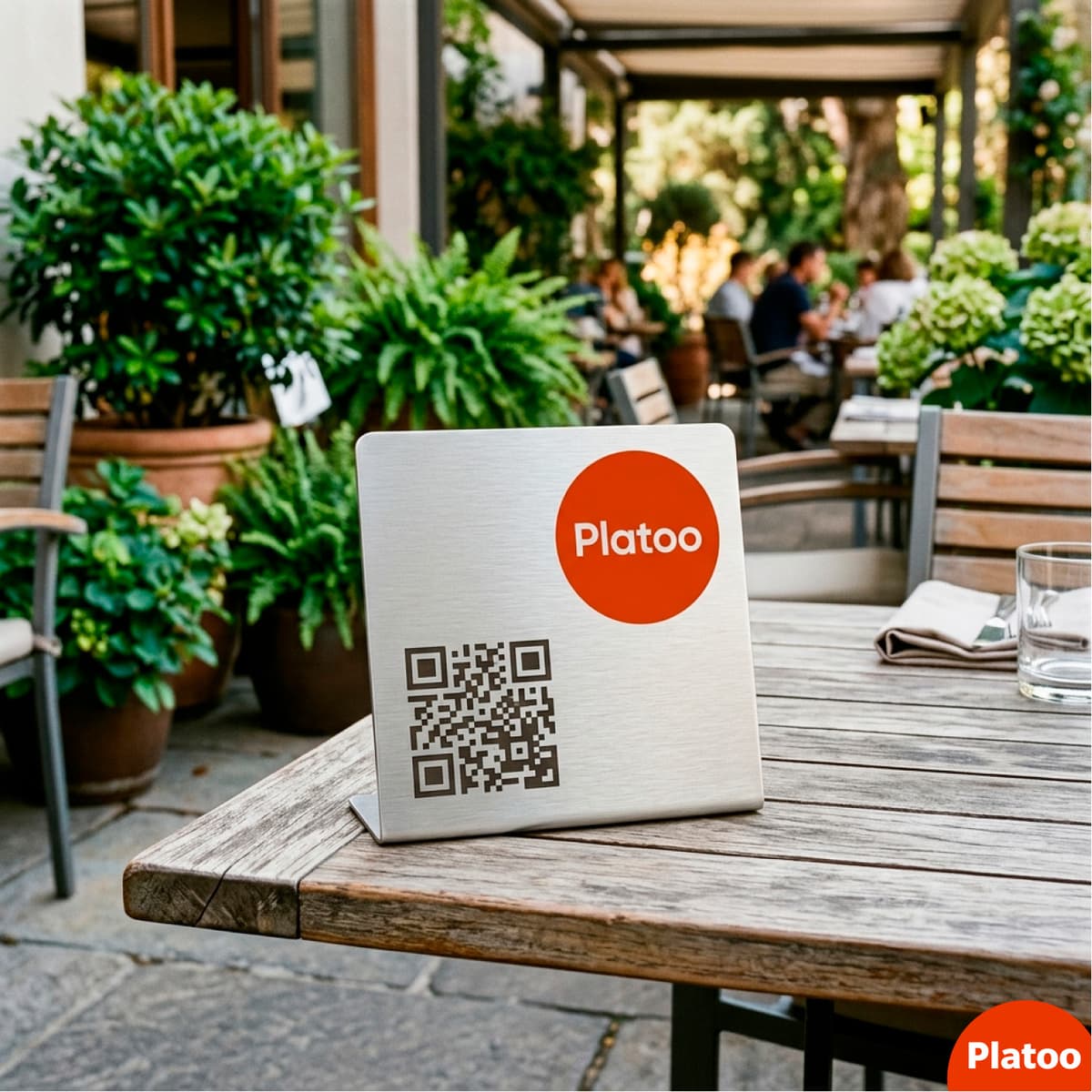 A sleek metal plate with an engraved Platoo QR code on a cafe's outdoor terrace table.